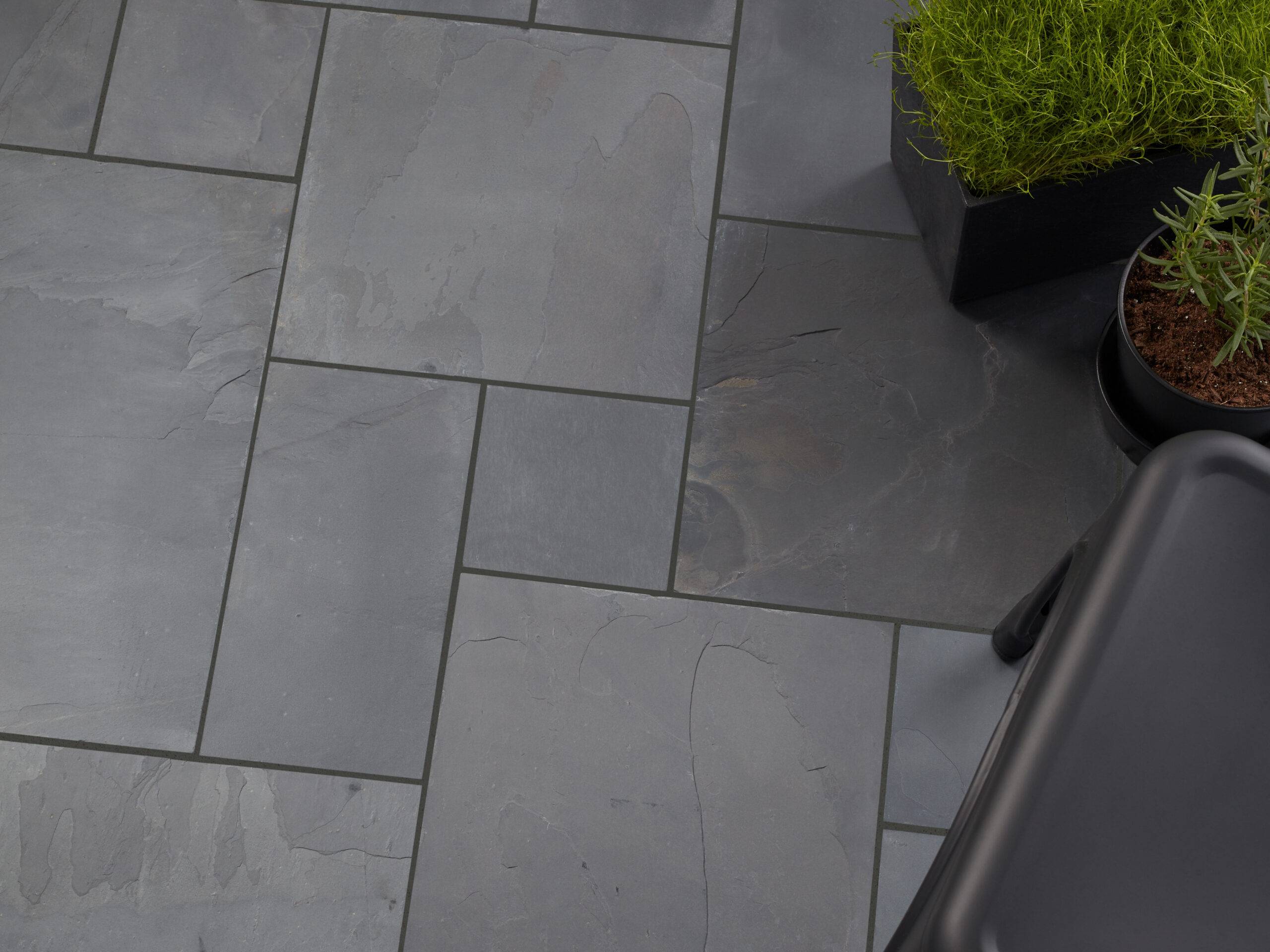 Outdoor patio paved with black slate Versailles patterned tile. A chair and plants are arranged on the patio.