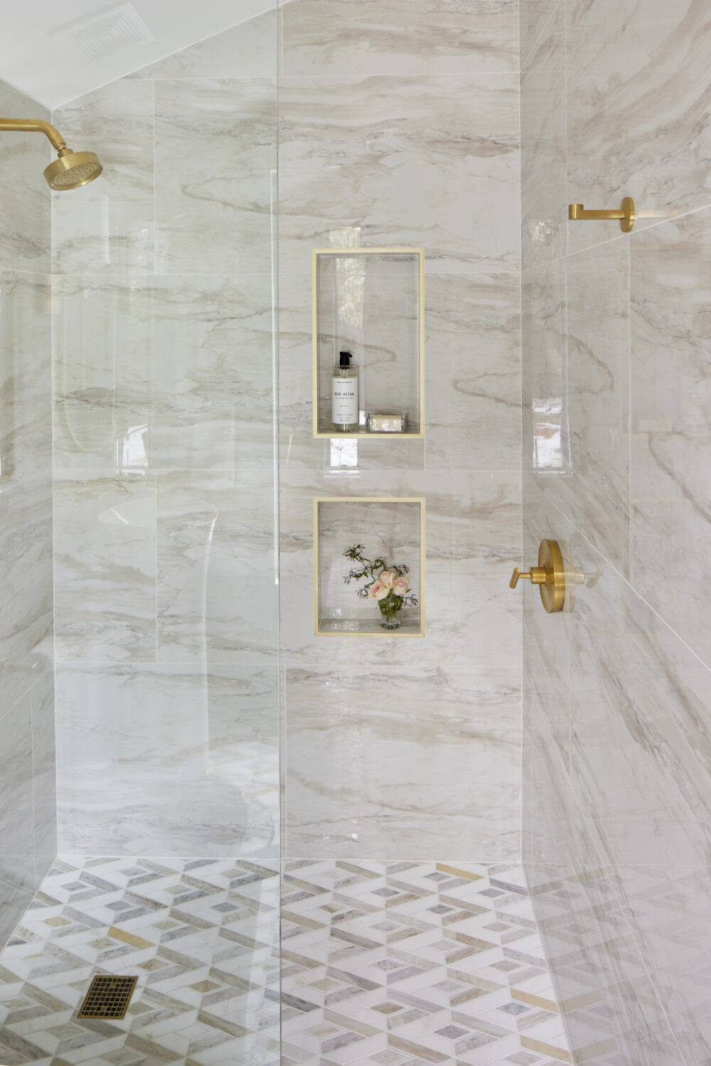 A shower wall with pink brick-look subway tile in a vertical offset pattern and shower niche trimmed with gold metal. 