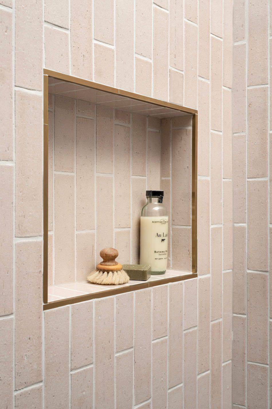 A shower niche featuring pink brick-look subway tile in a vertical offset layout and a rose-gold metal pencil liner. 