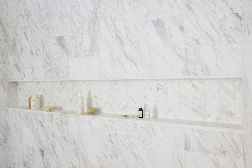 This beautiful white marble shower wall features a long recessed shelf. 