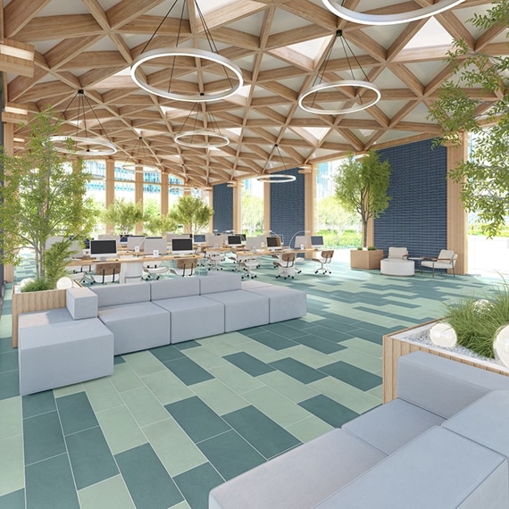 Library study area with light and dark green floor tile, blue wall tile, floor-to-ceiling windows, desks with computers and rolling chairs, and white sectional sofas.