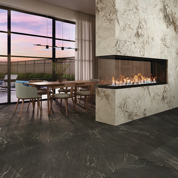 Modern dining room with black marble look tile flooring, open fireplace with cream & brown granite surround, table & chairs in front of glass sliding doors.